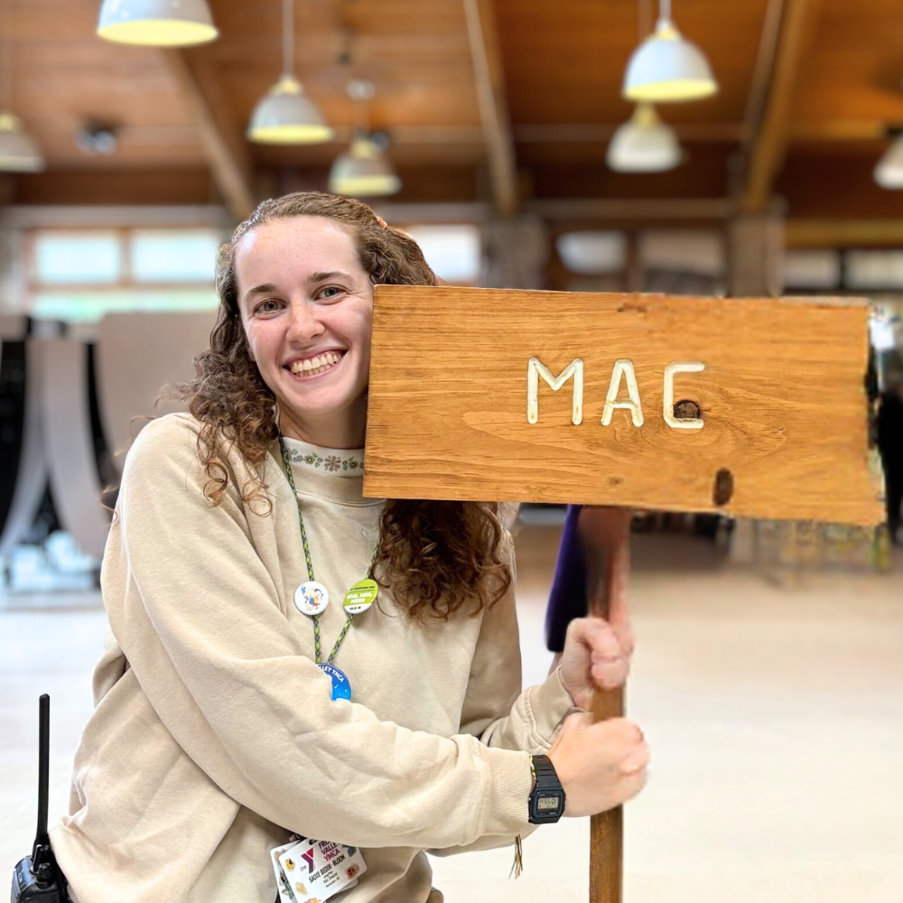 Sadie Bedik-Bloom holds a wooden sigh that says 'MAC'