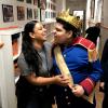 Evelyn and Ethan stand close to one another in a hallway, Ethan is smiling intensely while other people look on smiling