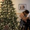 A profile view, Katherine stands behind Nick who is using a walker, they are to the right of the image with a Christmas tree to the left.