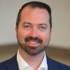 Headshot of Kevin Carey, he wears a deep blue suit and white button down shirt