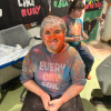 MSA student poses for camera, they are wearing a plastic cap and are covered in colorful powder