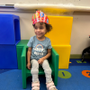 MSA student sits on a green plastic chair wearing a colorful cardboard crown