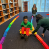MSA student sits on a wheeled toy and is being pulled along by a staff person