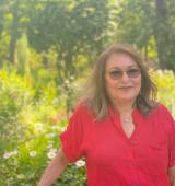 Person in red button-down shirt and sunglasses stands in front of a natural green space