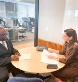 Two people sit at an office table practicing interview skills