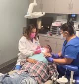 Kelvin is in the dental chair, fully reclined as the dentist cleans his teeth, he is holding hands with another clinician who sits on the other side of him