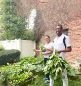 Two staff stand in Riverside Garden holding some of the veggies they've grown