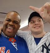 two men pose for photo, they are both wearing NY sports shirts