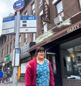 Lily stands at a bus stop in Brooklyn