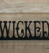 The word "WICKED" in a black fancy font on a wooden background