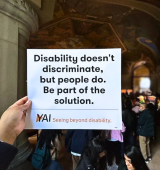 Someone holds up a rally sign at a rally in Albany "Disability doesn't discriminate, but people do. Be part of the solution."