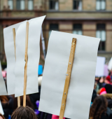 the back of 3 signs (no writing visible) at a protest
