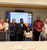 Group of people stand, sit and crouch together for a photo in a board room