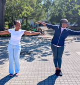 Two woman stand in a park with their arms out stretching