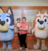 Elizabeth stands holding her daughter on her hip between Bluey and Bingo