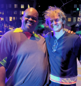 Kenneth stands with Tim, they are smiling and standing close together at night on a city street, with colorful event lighting and tall apartment buildings in the background.