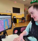 Amelia at her wheelchair, she is looking at the screen of the communication device she is using talk suite on