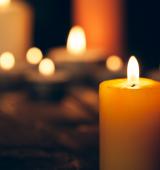 A burning candle in foreground with blurred burning candles behind it in on a black background