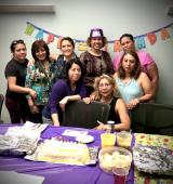 Group of people stand in front of bunting flags on wall and a table with food and a purple table cloth