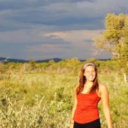 Kat Leonard stands outside to the right. She's wearing a red top and is surrounded by a vast amount of natural space behind her.