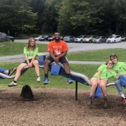 Group of people in a playground sitting on different parts fo an uneven balance bar