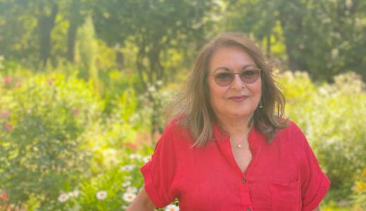 Person in red button-down shirt and sunglasses stands in front of a natural green space