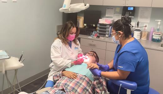 Kelvin is in the dental chair, fully reclined as the dentist cleans his teeth, he is holding hands with another clinician who sits on the other side of him