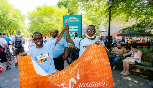 Diogeneis and a friend high-five each other while holding the CPC banner at the Central Park Challenge