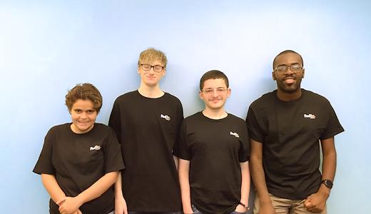 Group of 4 people stand leaning against a wall, all wearing black FedEx shirts and smiling for picture