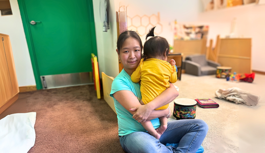 Mei-Feng sits cross legged on the floor of daycare while holding a baby