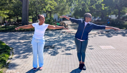Two woman stand in a park with their arms out stretching