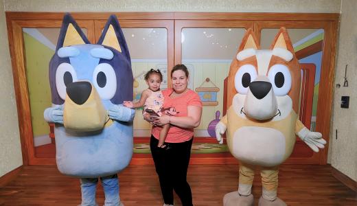 Elizabeth stands holding her daughter on her hip between Bluey and Bingo