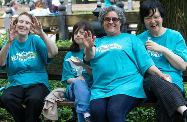 Group of people at a bench in central park they are smiling and dancing and wearing Central Park Challenge t-shirts