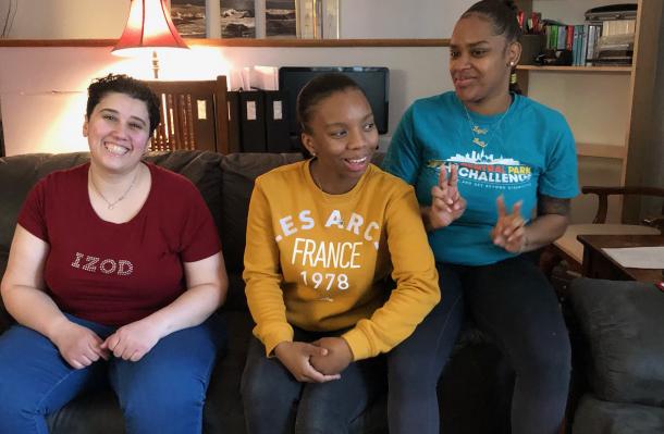 Three people sit on a couch in an NIPD/NJ home, they are looking in different directions and smiling