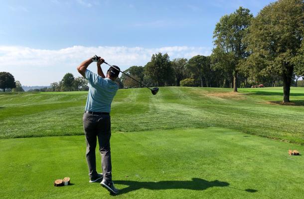 Person taking a swing with a golf club, you can see an expanse of the fairway ahead of them.