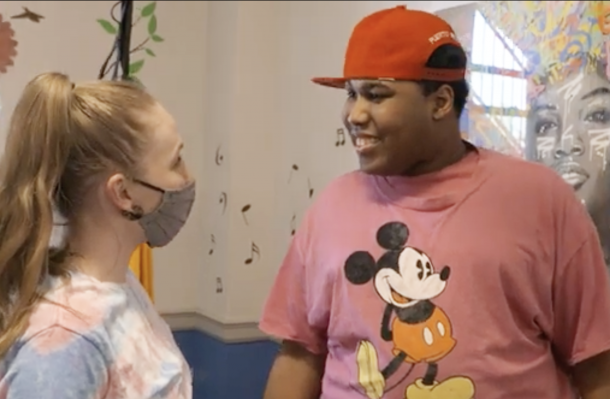 Two people stand in mid conversation. One has a red baseball cap and mickey mouse t-shirt