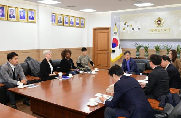 Group of people sit around a large conference table. Most are South Korean, Consuelo Senior from YAI also sits with them