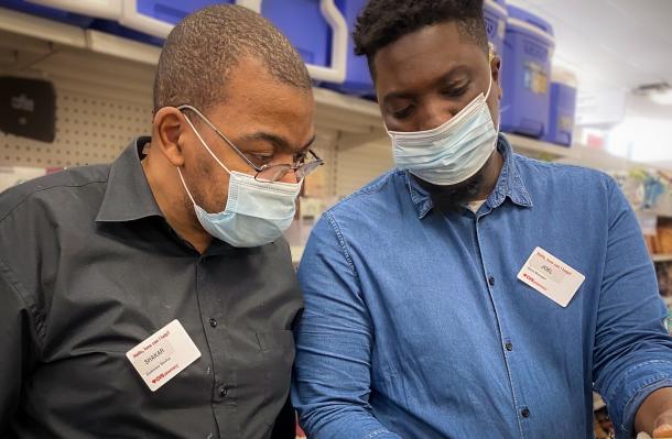 Shakar on left stands next to a CVS colleague on right, both wearing masks and looking at an item his colleague is holding