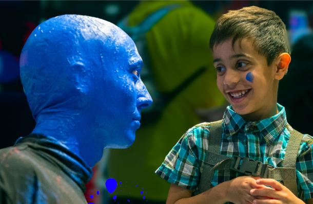 Member of Blue Man Group is next to a child who is smiling at them.