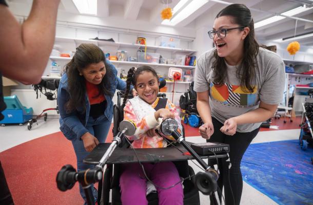 2 support staff are laughing with an iHOPE student who is a wheelchair.
