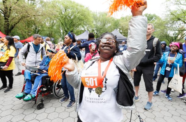 scene from the Central Park Challenge 2025. Person up front with pom poms celebrates at the event with a crowd of people behind them