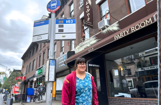 Lily stands at a bus stop in Brooklyn