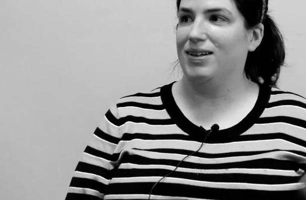 still from the Erase the R Word video. Woman with a lapel mic and striped shirt