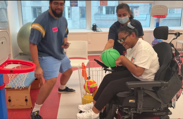 still from the video shows an iHOPE student at the iHOPE games laughs as she throws balls into a small baskeball hoop