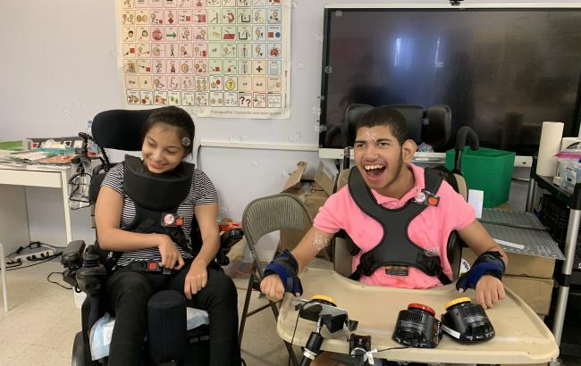 2 iHOPE students in classroom, both using wheelchairs and smiling for the photo