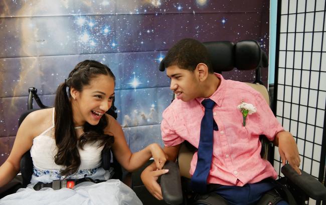 Jessica and Omar are both in wheelchairs right next to each other. It's prom and Omar is only looking at Jessica. The background is a large space/cosmic image.