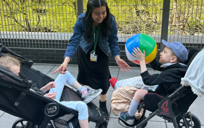 Two MSA students in adaptive strollers are outside playing catch with a beach ball, supported by a staff person in the middle