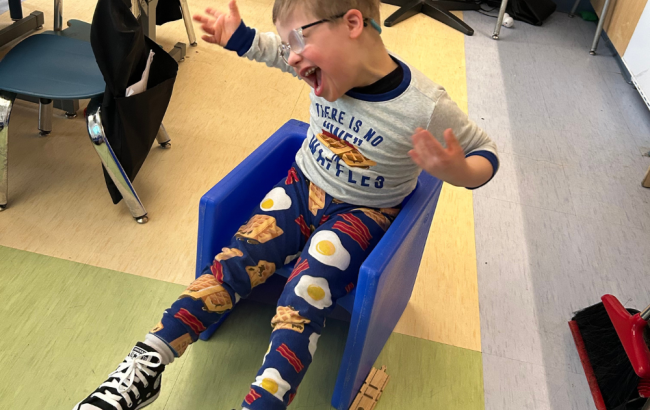 MSA student has arms in the air as they look excited while sitting on a blue plastic chair