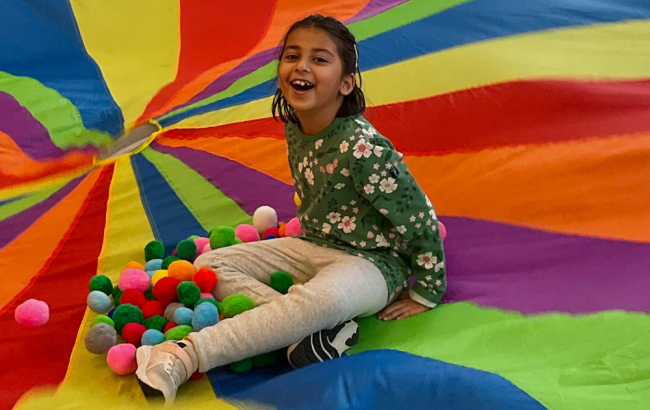 MSA student sits in the middle of a colorful parachute with colorful balls around them