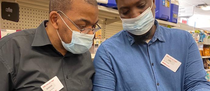 Shakkar on left stands next to a CVS colleague on right, both wearing masks and looking at an item his colleague is holding
